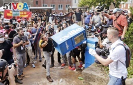FILE - In this Aug. 12, 2017 file photo, white nationalist demonstrators, right, clash with a counter demonstrator as he throws a newspaper box at the entrance to Lee Park in Charlottesville, Va.