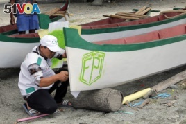 In this April 2, 2019, photo, a member of Islamic Defenders Front paints their group's logo as they help local fishermen to build boats at a fishing village affected by the 2018 tsunami in Palu, Central Sulawesi, Indonesia.