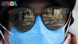 People are reflected on a volunteer's sunglasses outside a closed neighborhood alley following the coronavirus outbreak in Beijing, Sunday, March 1, 2020. (AP Photo/Andy Wong)