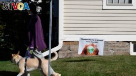 A woman walks her dog past a sign supporting equity in schools, in Guilford, Conn., on Tuesday, Oct. 19, 2021. (AP Photo/Jessica Hill)