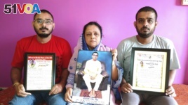 Anindita Mitra, 61, seen with her sons Satyajit Mitra, right and Abhijit Mitra, pose with portraits of her husband, Narayan Mitra, at her house in Silchar, India, Sunday, Sept. 13, 2020. (AP Photo/Joy Roy)