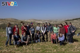 In this Friday, Jan. 25, 2019 photo, American rabbinical students take a group photo, with the village of Attuwani in the background, during a day planting olive trees, near Hebron in the West Bank. (AP Photo/Nasser Nasser)