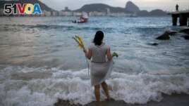 FILE - Many cultures have good luck charms or activities. In this photo, a woman offers flowers to Yemanja, goddess of the sea, for good luck in the coming year during New Year's Eve festivities on Copacabana beach in Rio de Janeiro, Brazil, Dec. 31, 2016. (AP Photo/Leo Correa)