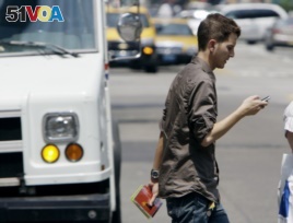 FILE - A man crosses a street in downtown Chicago while checking his phone.