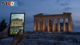 A man holds up a tablet showing a digitally overlayed virtual reconstruction of the ancient Parthenon temple, at the Acropolis Hill in Athens, Greece on Tuesday, June 13, 2023. (AP Photo/Petros Giannakouris)