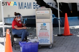 FILE - A poll worker wears personal protective equipment as she monitors a ballot drop box for mail-in ballots outside of a polling station during early voting, in Miami Beach, Florida. Aug. 7, 2020.