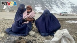 Gulnaz, left, keeps her 18-month-old son warm themselves as they wait for alms in the Kabul - Pul-e-Alam highway eastern Afghanistan, Tuesday, Jan. 18, 2022. (AP Photo/Kathy Gannon)