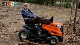 In this photo provided by Ed Smith, Geoffrey Holt rests his leg on top of his riding mower in Hinsdale, N.H., on April 4, 2020. Holt left the town of Hinsdale nearly $4 million when he died last June. (Ed Smith via AP)