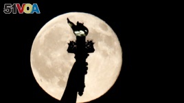 In this July 31, 2015, file photo, a blue moon rises behind the torch of the Statue of Liberty seen from Liberty State Park in Jersey City, N.J. A blue moon happens when the moon rises in its full stage twice during the same month. (AP Photo/Julio Cortez)