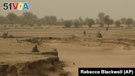People walk past a dry seasonal riverbed in the Matam region of northeastern Senegal.