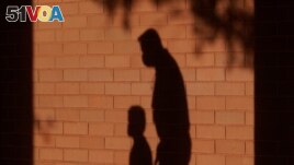 The shadow of an adult and a child is cast on the wall as they walk to a classroom in Davie, Florida, October 9, 2020. (AP File Photo) 