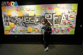 In this November 14, 2019, photo, a student attaches a note to the Resilience Project board on the campus of Utah Valley University, in Orem, Utah. The purpose of the project is to let students know that it is OK to struggle.