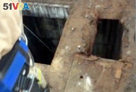 This photo from video provided by the Los Angeles Fire Department shows firefighters dropping a video camera down a large hole next to where a 13-year-old boy fell through through the small hole at right into a river of sewage in the Griffith Park area of