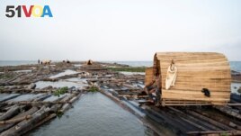 Egontoluwa Marigi, 61, sits in his shelter on his grouping of logs, while transporting the logs from Ondo State to Lagos State on the Lagos Lagoon, Nigeria on December 1, 2021. (REUTERS/Nyancho NwaNri)
