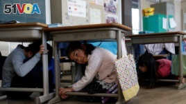 School children take shelter under desks during an earthquake simulation exercise in an annual evacuation drill at an elementary school in Tokyo, March 10, 2017.