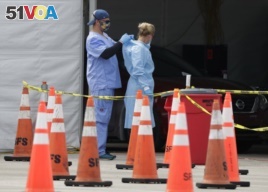 In this July 5, 2020, file photo, healthcare workers help each other with their personal protective equipment at a drive-thru coronavirus testing site outside Hard Rock Stadium in Miami Gardens, Fla.