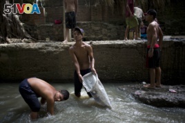 In this Nov. 30, 2017 photo, Douglas, center, holds a sack in the polluted Guaire River as he and others pull mud up from the bed of the river in search of gold and other valuables to sell, in Caracas, Venezuela.