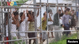 Asylum-seekers look through a fence at the Manus Island detention center in Papua New Guinea, March 21, 2014.