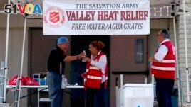 Salvation Army volunteer Francisca Corral, center, gives water to a man at a their Valley Heat Relief Station, Tuesday, July 11, 2023 in Phoenix. (AP Photo/Matt York)