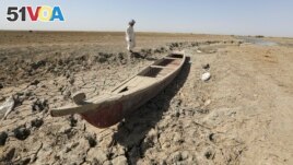 A fisherman stands next to his boat in a dry ground in the Chibaish marshes during low water levels in Nasiriyah of southern Iraq on June 16, 2022. (AP Photo/ Nabil al-Jurani)