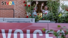 A couple wave from a window as they greet a bus delivering a loudspeaker message from family and friends in Brussels, Wednesday, April 22, 2020. (AP Photo/Olivier Matthys)