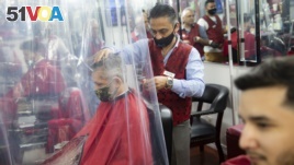 Peter Shamuelov, center, wears a protective mask as he gives a haircut to a customer at Ace of Cuts barbershop, Monday, June 22, 2020, in New York. For the first time in three months, New Yorkers will be able to dine out, though only at outdoor tables. (AP Photo/John Minchillo)