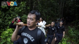 Members of a police forensic team carry a body bag with human remains dug from the grave near the abandoned human trafficking camp in the jungle close the Thailand border at Bukit Wang Burma in northern Malaysia May 27, 2015.