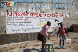 Two young girls sell groundnuts in front of an informational mural advising on precautions to avoid catching the new coronavirus, in the Kibera slum, or informal settlement, of Nairobi, Kenya Thursday, April 2, 2020.