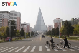 People wearing face masks cross a road in front of the Ryugyong Hotel in Pyongyang, North Korea Tuesday, April 28, 2020. (AP Photo/Cha Song Ho)