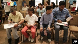 Derek Martinez, second from left, and Jason Victoria, second from right, watch as their fathers, Alex Martinez and Melvin Victoria place their certificates of citizenship in mounting folders after a ceremony at the Bronx Zoo, Tuesday, May 26, 2015, in New York. (AP Photo/Julie Jacobson)