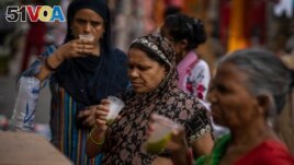 Shoppers drink juice in plastic glasses as they take a break at a weekly market in New Delhi, India, Wednesday on June 29, 2022. (AP Photo/Altaf Qadri)