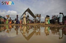 Rohingya refugees are reflected in a puddle during Eid al Adha celebration at Kutupalong refugee camp, Bangladesh, Wednesday, Aug. 22, 2018.