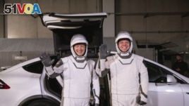 In this Friday, Jan. 17, 2020 photo made available by NASA, astronauts Doug Hurley, left, and Robert Behnken pose in front of a Tesla Model X car during a SpaceX launch dress rehearsal at Kennedy Space Center in Cape Canaveral, Fla. (Kim Shiflett/NASA)