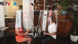 A man and a woman demonstrate dining under a plastic shield Wednesday, May 27, 2020 in a restaurant of Paris. (AP Photo/Thibault Camus)
