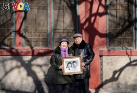 Huang Fusheng, right, 83, and his wife, Tang Lanfang, 80, pose with their wedding photo, taken in 1958, at Prince Fu Mansion built during Qing dynasty, where they worked together from 1965 to 1992, in central Beijing, China, Feb. 7, 2018.