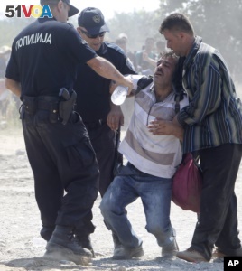 Macedonian police officers help a dehydrated migrant at the border from Greece to Macedonia, near southern Macedonian town of Gevgelija, on Monday, Aug. 31, 2015. (AP Photo/Boris Grdanoski)