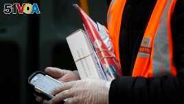 In this March 5, 2020, photo, a Royal Mail employee wears gloves as he hold parcels and the signature handheld as he delivers in London.