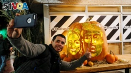 A man takes a selfie next to a giant pumpkin created by Master Carver Hugh McMahon with the faces of 2016 Democratic nominee Hillary Clinton and Republican presidential nominee Donald Trump at Chelsea Market in New York, U.S., October 28, 2016.