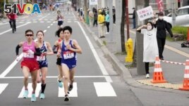 A spectator raises a paper sign reading 'It is impossible to hold the Olympics, face up to reality' along the race route during the half-marathon as part of Hokkaido-Sapporo Marathon Festival 2021.