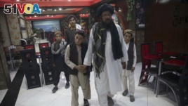 In this photo taken July 25, 2017, Mohammed Naseer, with black turban, holds his sons' hand when they enter a Pizza Restaurant in Kabul, Afghanistan. Mohammed Naseer spent several weeks arranging for his son, a nephew and several other children from his d