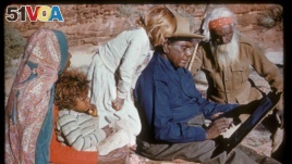 An undated photo released Oct. 14, 2017, shows family members watching Australia's most famous Aboriginal artist, Albert Namatjira, sitting on a rock as he paints.