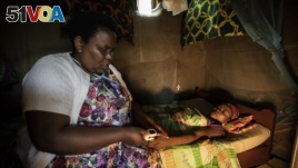 In this photo taken Tuesday, Nov. 5, 2019, palliative care nurse Madeleine Mukantagara, 56, left, uses a pulse-oximeter to check on the health of Vestine Uwizeyimana, 22, right, who has spinal degenerative disease and is taking oral liquid morphine.