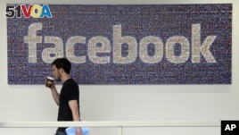  In this March 15, 2013, photo, a Facebook employee walks past a sign at Facebook headquarters in Menlo Park, Calif.