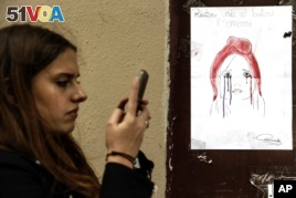 A woman checks her smartphone by a poster showing a weeping image of Marianne, symbol of the French Republic, near Le Carillon restaurant, a site of terrorist attacks, in Paris, Nov. 17, 2015. The attacks have triggered waves of social media communication