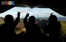 In this photo provided by the U.S. Air Force, Japan Air Self-Defense Force airmen wave at residents of the Commonwealth of the Northern Marianas island of Pagan as they drop a package to the islanders as part of Operation Christmas Drop.