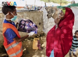 In this photo taken Wednesday, June 10, 2020, an internally-displaced Somali woman, right, is informed how to protect herself from the coronavirus, at the Weydow IDP camp in Mogadishu, Somalia. (Hamza Osman/International Organization for Migration (IOM)