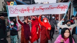Youth activists and Buddhist monks participate in an anti-military government protest rally while holding a banner that reads in Burmese, Who dares to stay on the opposite side of the people's will, on Tuesday, Feb. 1, 2022, in Mandalay, Myanmar. The ne