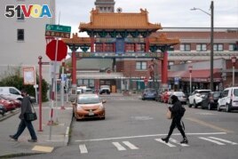 Pedestrians walk near the main entrance to Seattle's Chinatown-International District Thursday, March 18, 2021. (AP Photo/Ted S. Warren)