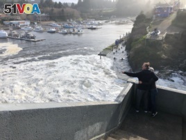 In this Jan. 11, 2020 photo residents watch as an extreme high tide rolls in and floods parts of the harbor in Depoe Bay, Oregon, USA. (AP Photo/Gillian Flaccus)