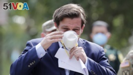 Florida Gov. Ron DeSantis puts on a protective face mask during a news conference at the Urban League of Broward County, during the new coronavirus pandemic, Friday, April 17, 2020, in Fort Lauderdale, Fla. (AP Photo/Lynne Sladky)